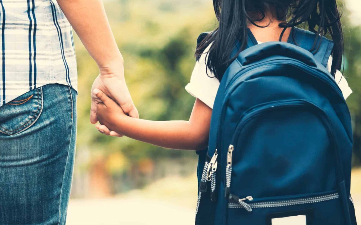 A parent holding a child's hand on the way to school