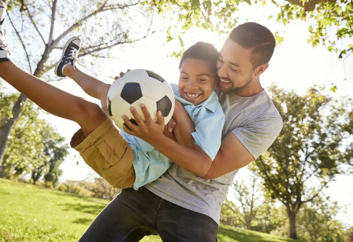 A dad lifting his laughing son, who is holding a football