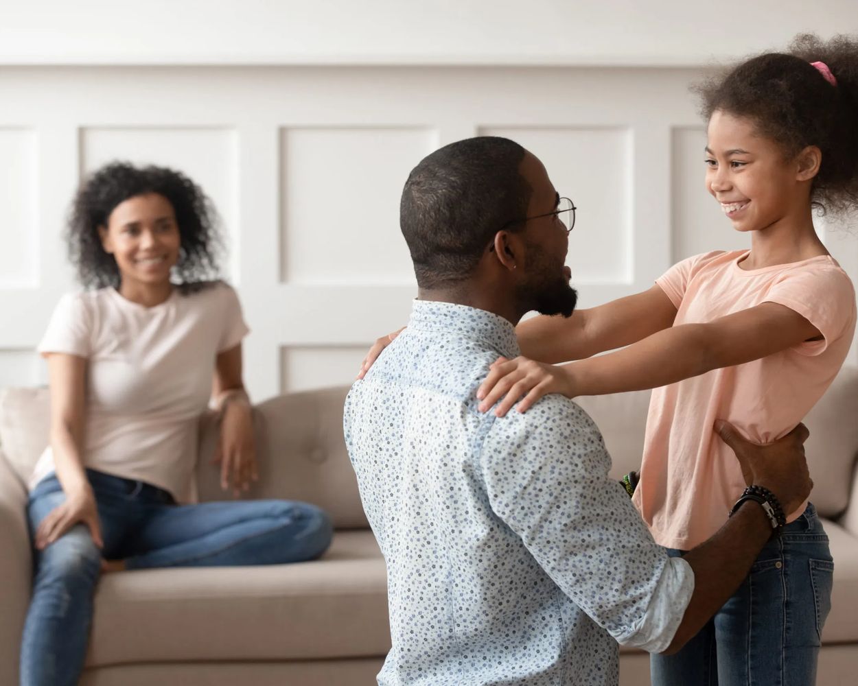 A dad greeting his daughter while her mum smiles from the sofa