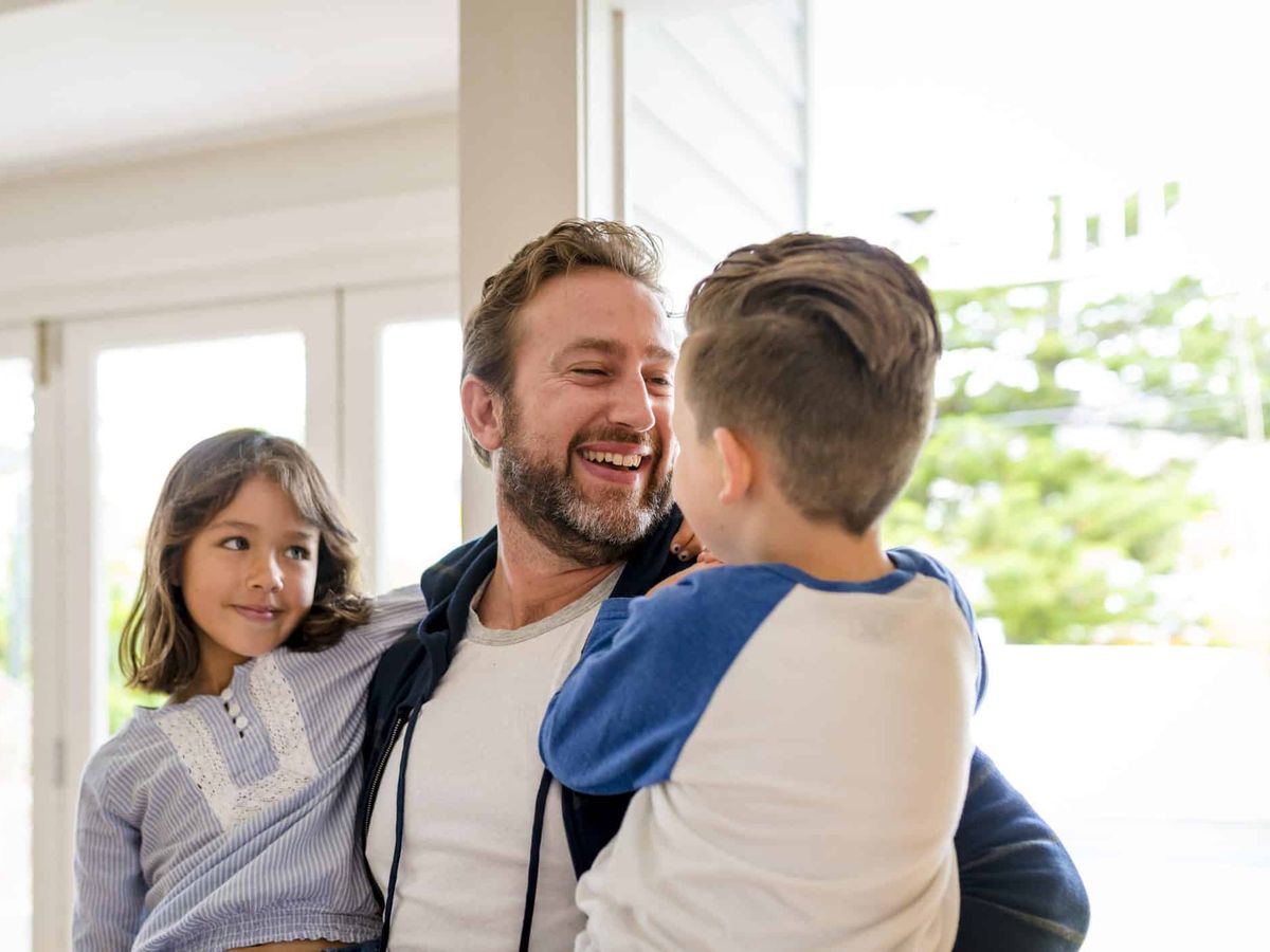 A dad holding his son and daughter, all three smiling